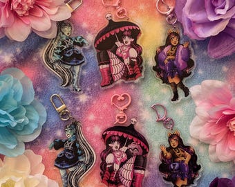 May include: A collection of acrylic keychains featuring colorful illustrations of anime-style characters. The keychains have various designs, including characters with long hair, dresses, and accessories. Each keychain has a metal clasp for attachment.