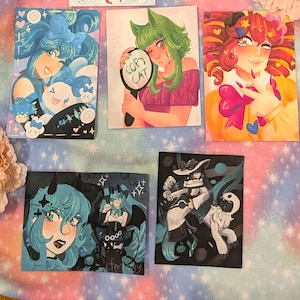 May include: Five colorful art prints featuring anime-style illustrations. The prints showcase various characters with vibrant hair and clothing. One print has the text "COPY CAT" on a mirror. The art style is detailed with bold colors and expressive features.