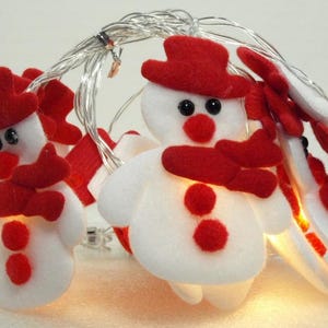 May include: A string of white LED lights with red felt snowman ornaments. Each snowman has a red hat, scarf, and buttons.