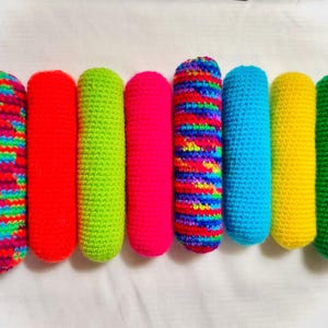 May include: A set of ten colorful crocheted cylinders, each with a different color and pattern. The colors include pink, red, green, blue, yellow, and purple.