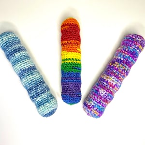 May include: Three handmade crochet cozies in a vertical orientation. One is blue and white, one is rainbow-colored, and the third is purple, pink, and blue. The cozies are cylindrical and appear to be made of yarn.