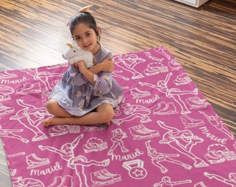 May include: A bright pink fleece blanket featuring a repeating white line-art pattern of ice skaters, ice skates, and medals, with the name Mariel printed in a cursive script throughout the design, creating a cohesive and repetitive graphic motif.