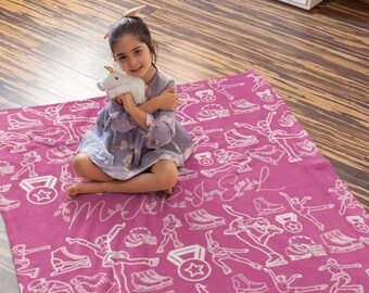 May include: Pink fleece blanket with a white design of figure skaters and medals. The blanket has the name "Marisa" written in cursive on it.