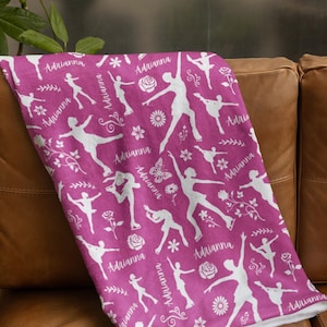 May include: A pink fleece blanket with a white silhouette pattern of figure skaters, flowers, and butterflies. The name "Adrianna" is repeated throughout the pattern.