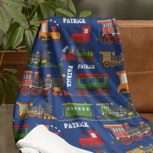 May include: A blue fleece blanket with a repeating pattern of colorful toy trains. The blanket features the name "Patrick" repeated throughout the design.