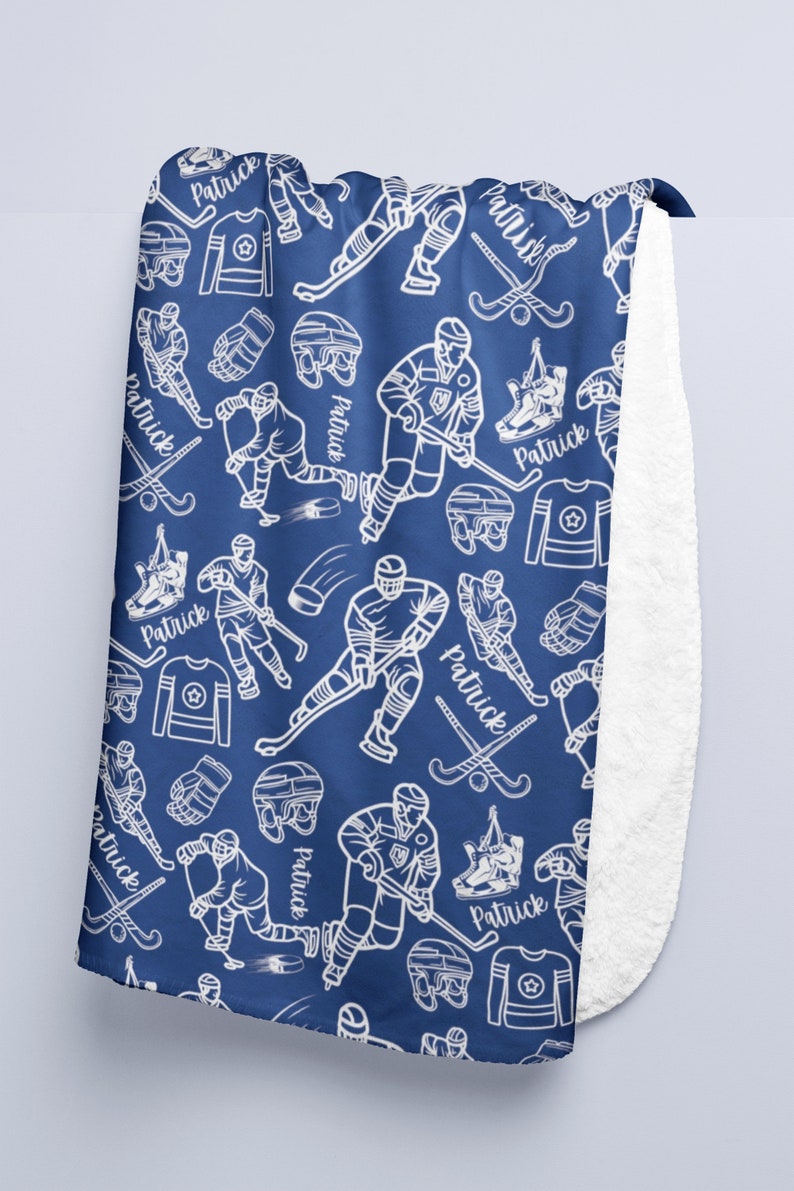 Pu&ograve; includere: Una coperta in pile blu con un motivo di giocatore di hockey bianco. Il motivo include bastoni da hockey, puck e il nome "Patrick" ripetuto in tutto.