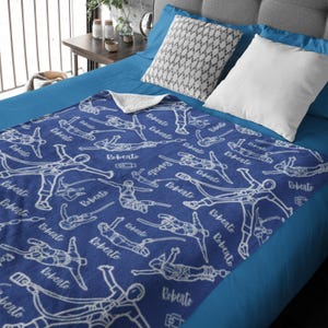 May include: A blue fleece blanket featuring a repeating white line-art pattern of individuals wearing climbing harnesses and ropes, interspersed with the name Roberto written in a cursive script across the entire surface of the fabric.
