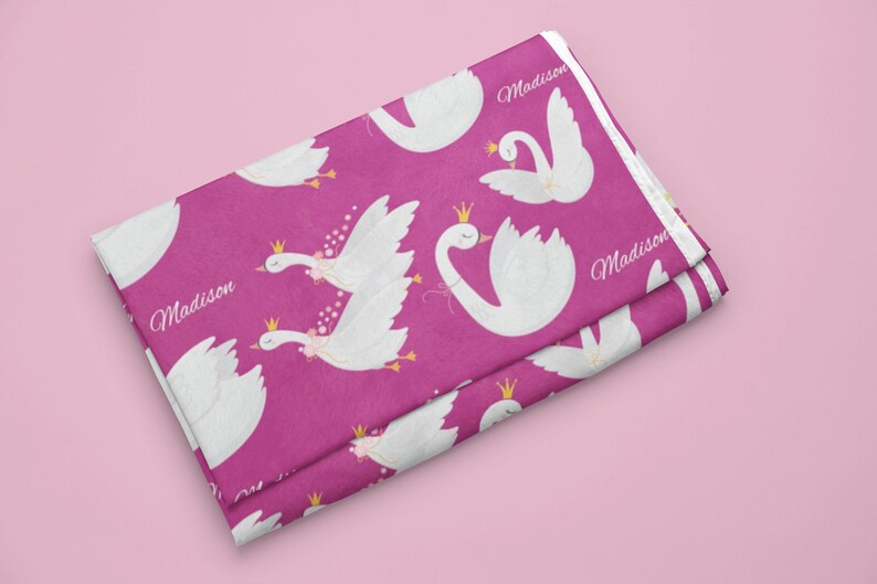 May include: Pink fabric with a white swan pattern. The swans are wearing crowns and have pink flowers. The fabric says "Madison" on it.