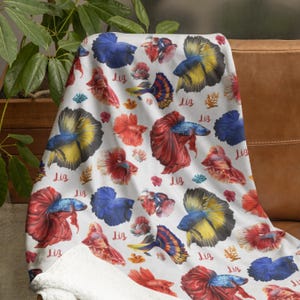 May include: White fleece blanket with a colorful pattern of betta fish and the word "Liz" repeated throughout.
