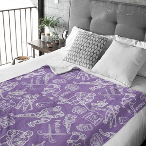 Pu&ograve; includere: Coperta in pile viola con un motivo di giocatore di hockey bianco. La coperta presenta un motivo ripetuto di giocatori di hockey, puck, bastoni e il nome "Patrick".