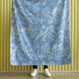 Pu&ograve; includere: Una coperta in pile blu con un motivo di giocatore di hockey bianco. La coperta presenta il nome "Patrick" ripetuto su tutto il design.