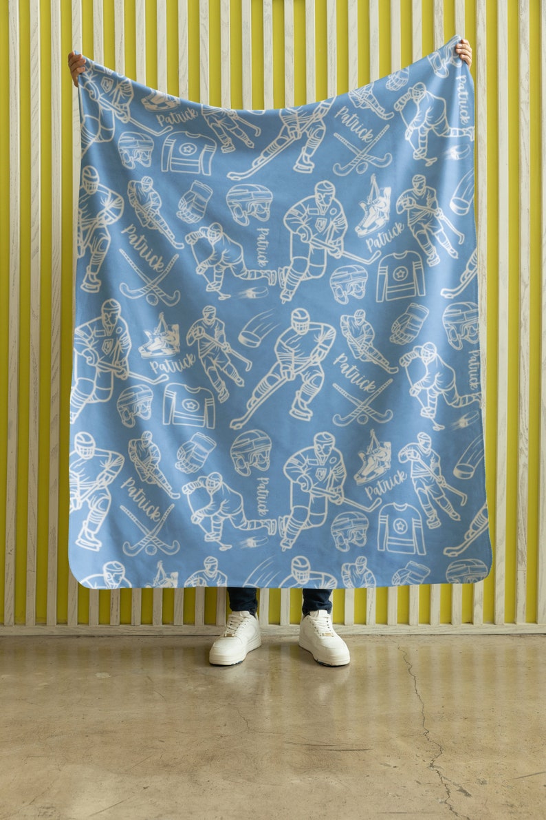 Pu&ograve; includere: Una coperta in pile blu con un motivo di giocatore di hockey bianco. La coperta presenta il nome "Patrick" ripetuto su tutto il design.