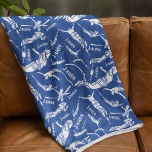 May include: A blue throw blanket featuring a repeating white pattern of figures bungee jumping and the name Laura printed in a cursive script throughout the fabric. The blanket has a soft texture and a white underside visible at the folded edge.