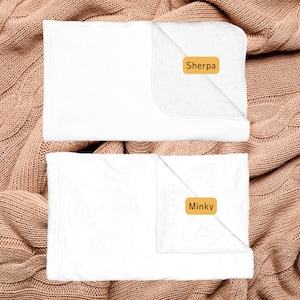 May include: Two white blankets, one labeled "Sherpa" and the other labeled "Minky", are displayed on a brown knitted surface.
