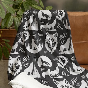 May include: A black and white throw blanket featuring a repeating pattern of wolves, pine trees, and full moons. The design includes the name Tim in a cursive script and claw mark graphics. The blanket has a soft, white, textured fleece lining.
