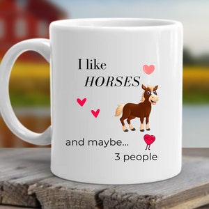 May include: White ceramic mug with a brown cartoon horse and the text "I like horses and maybe... 3 people" with pink hearts.