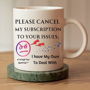 Könnte beinhalten: Weiße Keramiktasse mit einer schwarzen und roten Grafik, auf der "PLEASE CANCEL MY SUBSCRIPTION TO YOUR ISSUES, I have My Own To Deal With" steht. Die Grafik enthält auch ein Comic-Gesicht mit einem wütenden Ausdruck und einem Blitz.