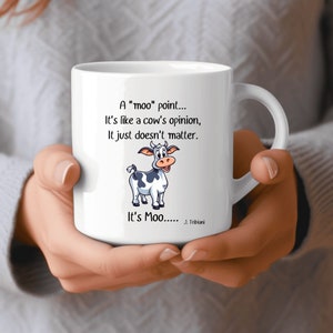 Peut inclure: Mug en céramique blanche avec une illustration de vache humoristique et le texte "A 'moo' point... It's like a cow's opinion, It just doesn't matter." Le mug porte aussi l'inscription "It's Moo..... J. Tribiani."