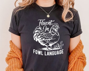 May include: Black t-shirt with a white graphic of a rooster and the text "Fluent in Fowl Language".