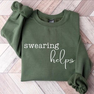 May include: A green sweatshirt with the text "swearing helps" printed in white on the front.