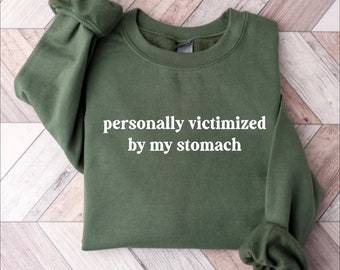 May include: A green sweatshirt with the text "personally victimized by my stomach" in white.
