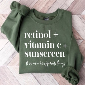 May include: A green sweatshirt with white text that reads "retinol + vitamin c + sunscreen there are a few of favorite things".