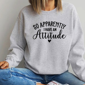 May include: A grey sweatshirt with the text "So Apparently I Have An Attitude" in black lettering with a small black heart below the text.