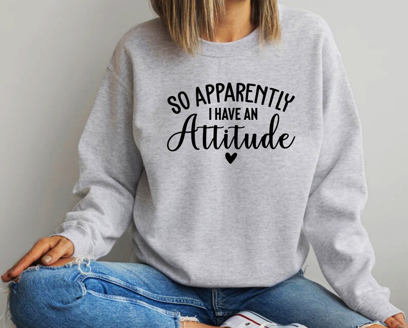 May include: A grey sweatshirt with the text "So Apparently I Have An Attitude" in black lettering with a small black heart below the text.