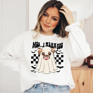 May include: White sweatshirt with a black and white checkered pattern, bats, and a ghost with a cow's head. The text "Moo... I mean Boo" is printed on the shirt.