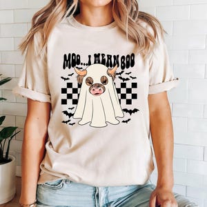May include: A white t-shirt with a black and white checkered pattern and a ghost with a cow's head. The text "Moo... I mean Boo" is printed on the shirt.