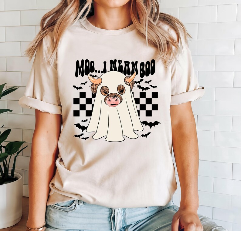 May include: A white t-shirt with a black and white checkered pattern and a ghost with a cow's head. The text "Moo... I mean Boo" is printed on the shirt.