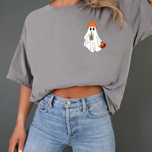 May include: A gray t-shirt with a ghost wearing an orange hat and holding a coffee cup. The ghost is holding a small orange pumpkin.