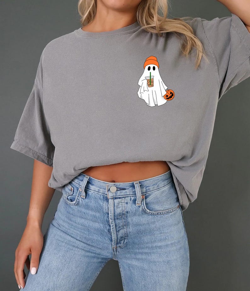 May include: A gray t-shirt with a ghost wearing an orange hat and holding a coffee cup. The ghost is holding a small orange pumpkin.