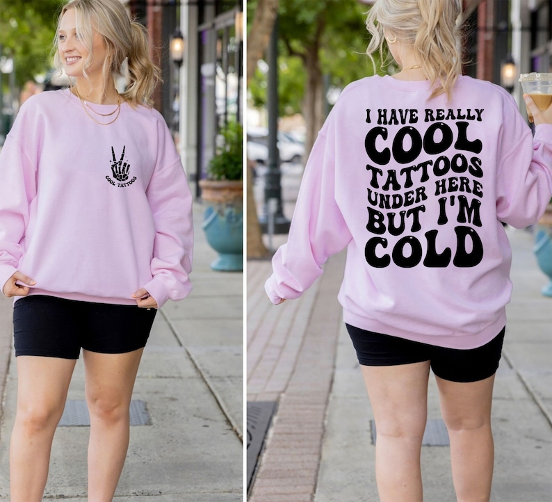 May include: Pink sweatshirt with a peace sign and the text "Cool Tattoos" on the front and the text "I have really cool tattoos under here but I'm cold" on the back.