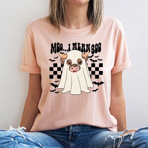 May include: A pink t-shirt with a black and white checkered pattern and a ghost cow with the text "Moo... I mean Boo" on it.