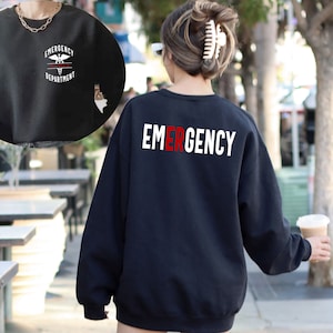 May include: Black sweatshirt with the word "EMERGENCY" printed in white on the back. The letter "E" is in red. The front of the sweatshirt has a white graphic of a medical symbol with the words "EMERGENCY DEPARTMENT" printed below it.