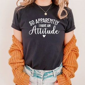May include: Black t-shirt with white text that reads "So Apparently I Have An Attitude" with a small white heart below the text.