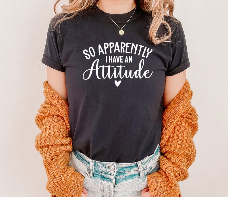 May include: Black t-shirt with white text that reads "So Apparently I Have An Attitude" with a small white heart below the text.