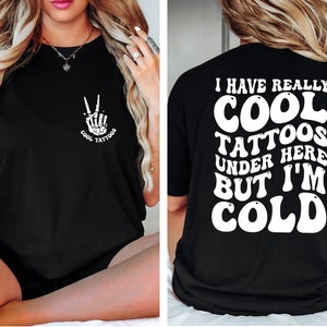 May include: Black t-shirt with a white graphic on the front that says "Cool Tattoos" and a skeleton hand making a peace sign. The back of the shirt has white text that says "I have really cool tattoos under here but I'm cold."