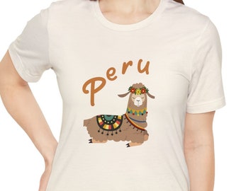 Puede incluir: Camiseta color crema con una llama de dibujos animados con una colorida montura y corona floral. La palabra "Peru" está escrita encima de la llama en escritura marrón. La camiseta la lleva una persona.