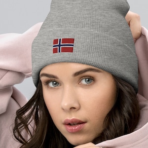 May include: A gray beanie with a small embroidered Norwegian flag on the front. The beanie is being worn by a person with long brown hair.