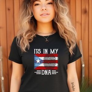 Puede incluir: Camiseta negra con un diseño de bandera puertorriqueña desgastado y el texto "ITS IN MY DNA".