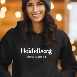 May include: Black hooded sweatshirt with white text that reads "Heidelberg 49.3988° N, 8.6724° E".