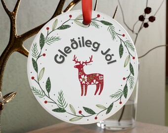 Könnte beinhalten: Runder weißer Weihnachtsbaumschmuck mit rotem Band. Der Anhänger zeigt einen grünen Kranz mit roten Beeren und ein stilisiertes Rentier mit einem rot-weiß gemusterten Körper. Der Text "Gleðileg Jól" ist in Schwarz innerhalb des Kranzes geschrieben.