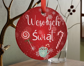 Op de afbeelding: Ronde rode kerstbal met de Poolse zin "Wesołych Świąt", wat in het Nederlands "Vrolijk Kerstfeest" betekent. De kerstbal heeft een snoepstok, een lolly en een kopje warme chocolademelk met marshmallows.