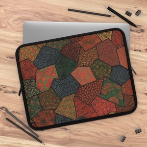 Puede incluir: Una funda para portátil con un diseño de patchwork que presenta varias formas geométricas y patrones en tonos de rojo, naranja, verde y azul.