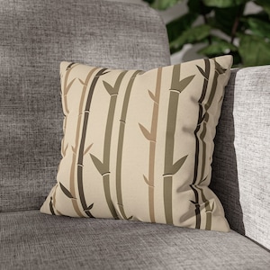 May include: A beige throw pillow with a brown and green bamboo print. The pillow is on a gray couch.