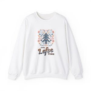 Puede incluir: Sudadera blanca con un dise&ntilde;o floral colorido y un &aacute;rbol en el centro. El texto "It's Lefse Time" est&aacute; impreso debajo del dise&ntilde;o.