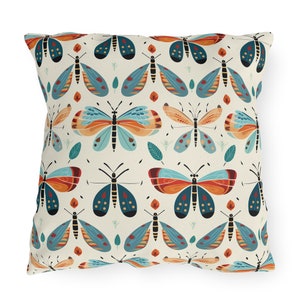 May include: Square throw pillow with a repeating pattern of stylized butterflies in shades of orange, teal, and black on a cream background. The butterflies are interspersed with small leaf and plant designs. The pillow is a decorative home accent.