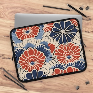 Pode incluir: Uma capa para laptop com um padrão floral. O design apresenta flores vermelhas, azuis e brancas sobre um fundo creme.